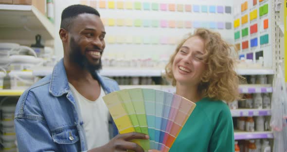 Young Smiling Diverse Couple Choosing Color for Walls in Hardware Store