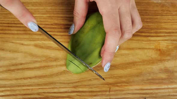 Female Hands Cut Avocado in Pieces on a Wooden Plank