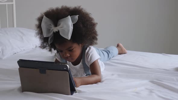 African girl lying on bed, using digital tablet alone.
