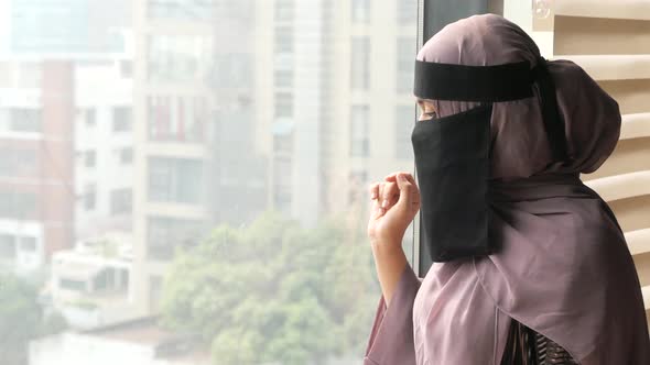 Young Muslim Women Covering Face Looking Through Window Indoor