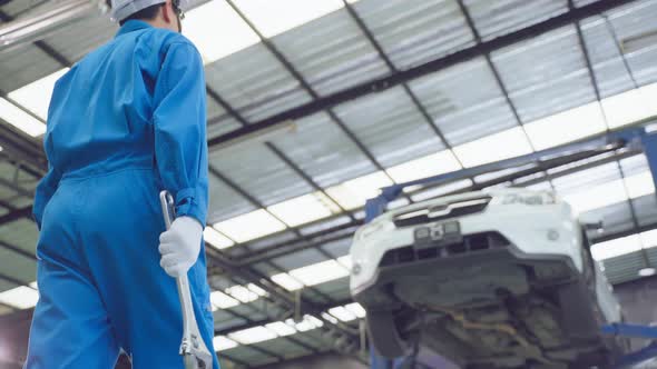 Asian automotive mechanic repairman look under car condition in garage.