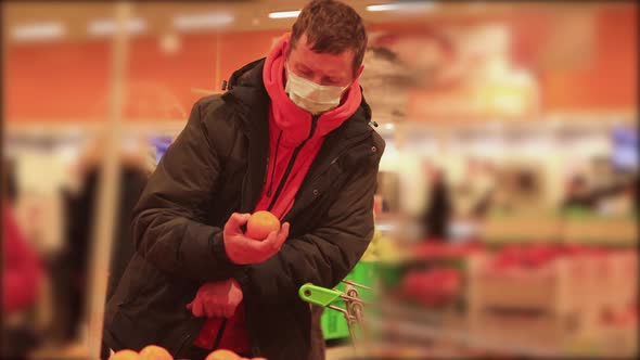 A Man with a Trolley in a Supermarket Picks Fruits with a Mask on His Face