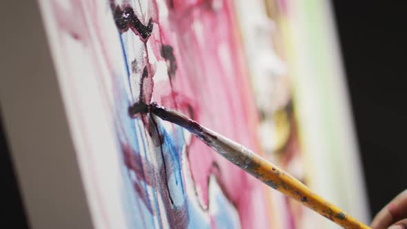 Close up of hand of male artist painting with paint brush on canvas at art studio