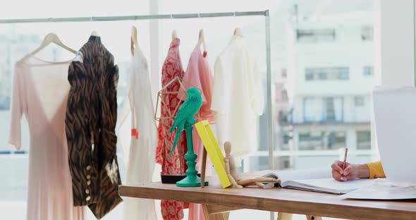 Fashion designer writing in book on desk 4k