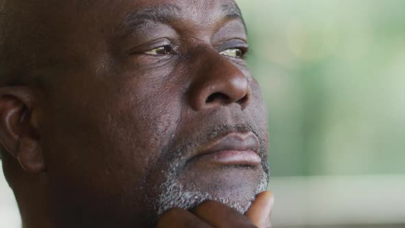 Thoughtful african american senior man holding chin looking out of window and smiling