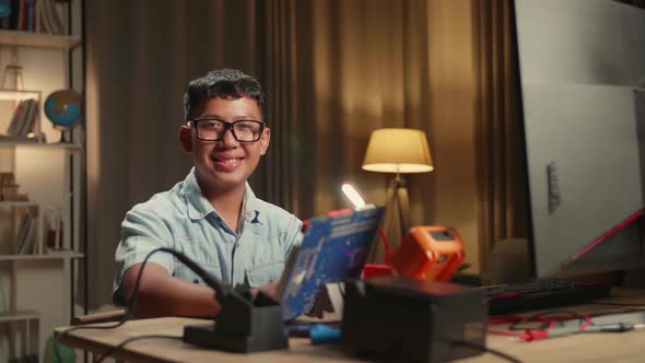 It Asian Boy Is Working With Desktop Computer And Main board In Home. He Turns And Warmly Smiles