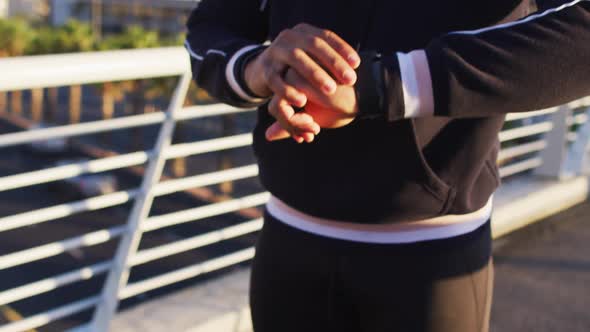 Midsection of african american man exercising on footbridge in city, checking smartwatch