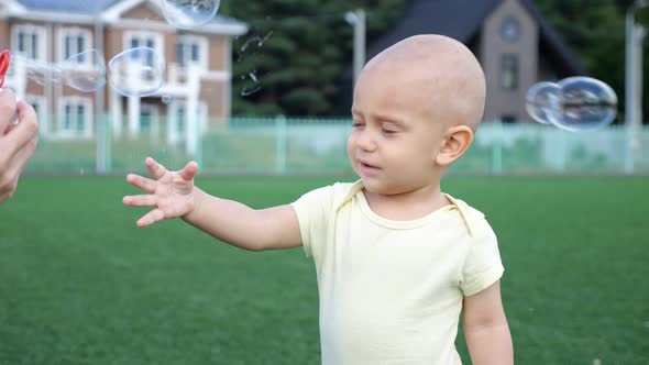 Toddler Boy Tries to Catch Bubbles Standing on Green Grass