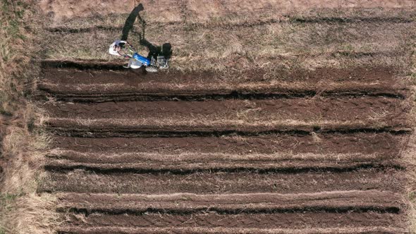 AERIAL - Man working a field with a rototiller, agriculture, wide shot tilt up