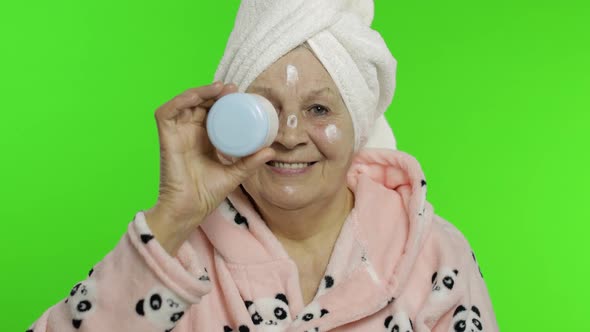 Elderly Grandmother in Bathrobe. Old Senior Woman with Moisturizing Cream Jar