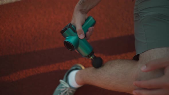 A Male Athlete Massages Muscles and Tendons with a Massage Percussion Device After a Workout at the