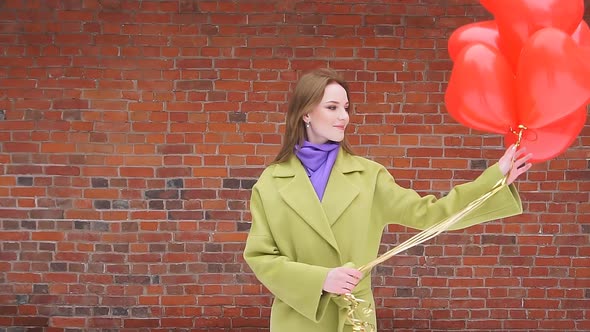 Stylish Lady in a City Park Turns Around Holding Balloons in Her Hands