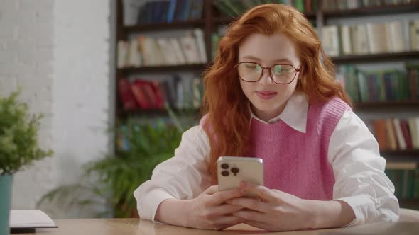 Attractive Student Woman Holding Modern Smartphone Texting Message in Home Office or Library alt
