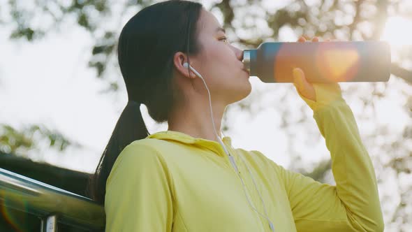 A beautiful caucasian woman athlete drinks water after running at the park.