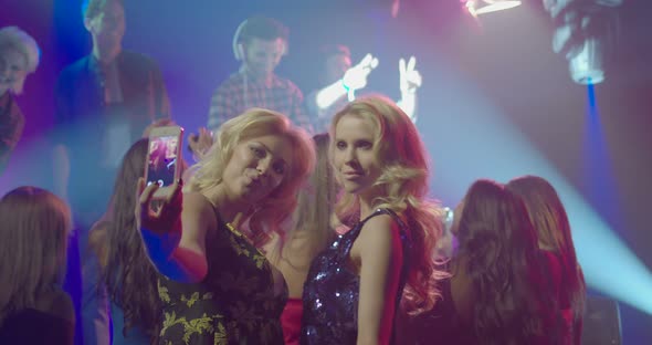 Female friends taking self photograph with mobile phone while enjoying music in nightclub