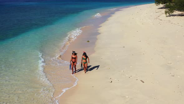 Girls with bikini wearing snorkel set with tube, mask and holding fins, walking on sandy beach, sear