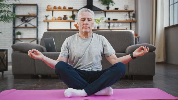 Elderly Male in Sportswear is Practicing Yoga in Lotus Position with Gyan Mudra on Pink Mat at at