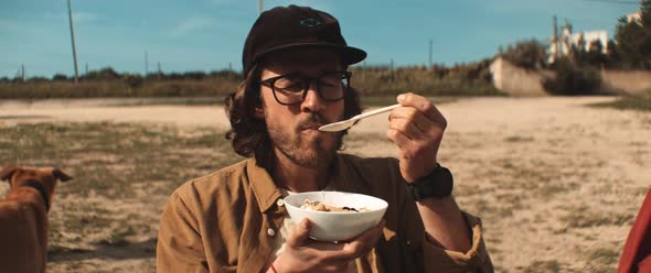 Young man eating from a bowl outdoors on camp site