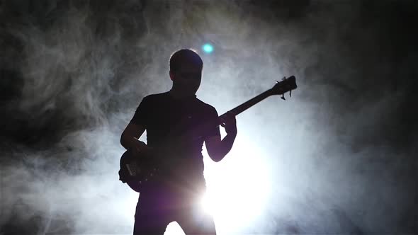 Slow Motion. Silhouette Bass Guitarist Man in Smoke. Black Background