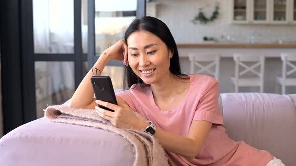 An Attractive Young Asian Woman is Using a Smartphone Indoor