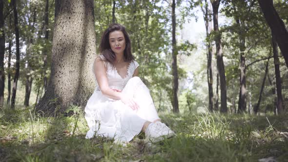 Portrait Cute Young Girl with Long Brunette Hair Wearing a Long White Summer Fashion Dress Sitting