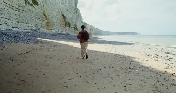 A Young Woman Runs Along a Pebbly Beach Past Sheer Chalk Cliffs