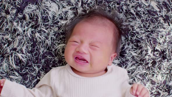 Top view happy newborn baby lying on a carpet looking at camera