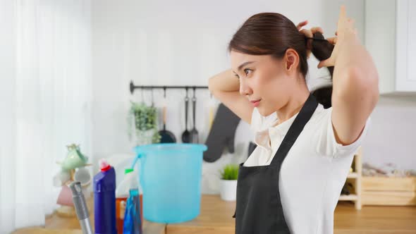 Portrait of Asian young cleaning service woman worker tying hair before working by doing housework.