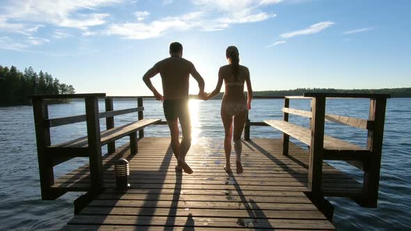 Couple Running on a Wooden Pier and Jumping Into the Lake