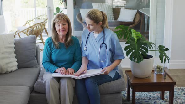 Female health worker assisting senior woman to read braille book