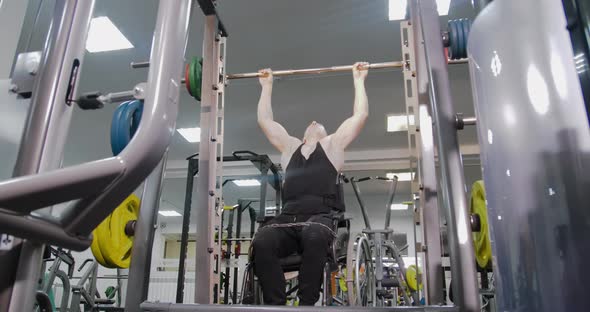 Disabled person in a wheelchair pulls up on a horizontal bar in the gym.