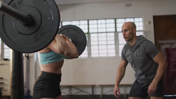 Fit caucasian woman working out with barbell with male trainer at the gym