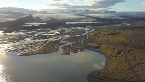 Aerial dolly out of fiords and lake in lowlands, Breiðamerkurjökull glacier in background on a cloud