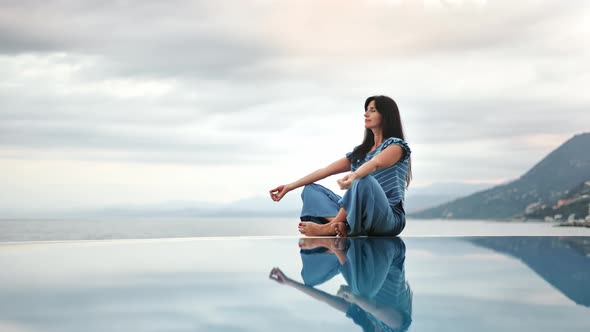 Happy Woman in Lotus Position Meditating at Endless Swimming Pool Sea Dramatic Sky Harmony Balance