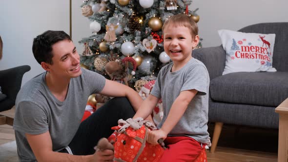 Little Boy Riding a Rocking Horse Near Xmas Tree