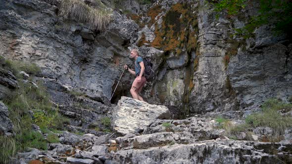 Man Hiker with a Backpack and Trekking Poles is Walking in the Rocky Mountains