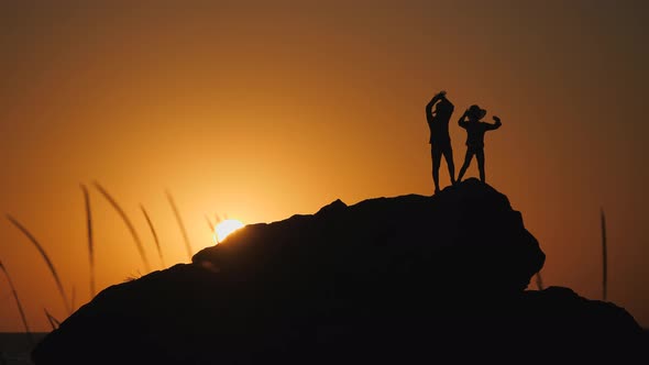 Children Silhouettes Against the Sunset, Boys in Hats with Brims Stand on a Rock