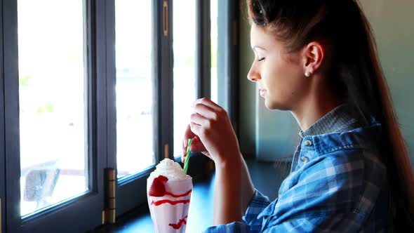 Happy woman looking through window while drinking milkshake