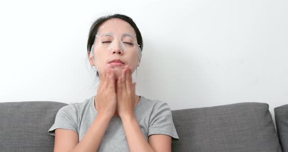 Woman applying paper sheet mask on face