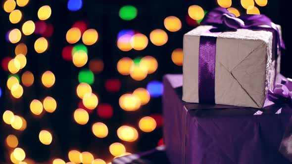 Beautifully Wrapped Gifts with Purple Ribbons. Presents on Bokeh Lights or Glowing Garlands