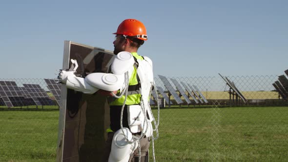 Male Technician in Exoskeleton Carrying Photovoltaic Panel