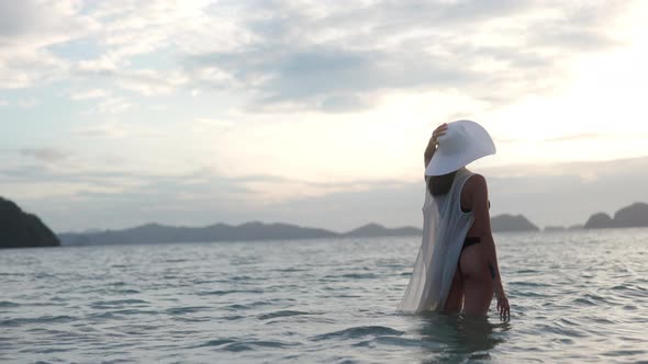 Woman In Thong Standing In Sea As Sun Sets