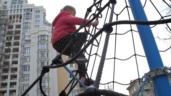 Junior Schoolgirl in Jacket and Leggings Climbs Up Rope Net