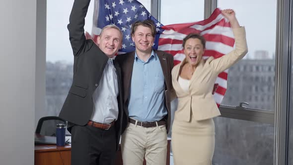 Cheerful American Business Team Posing with National Flag in Office