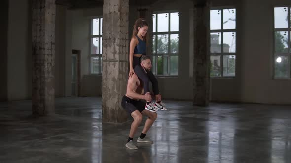 Athletic Shirtless Man Crouches with a Girl on His Shoulders in Empty Loft Studio