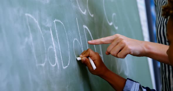 Teacher assisting schoolboy in writing alphabet on chalkboard