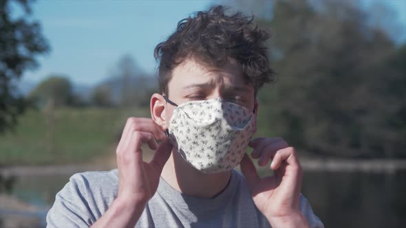 Young man puts on homemade white cotton corona virus mask MID SHOT