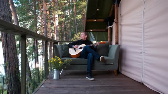 Man Sitting on Sofa Playing Guitar in Glamping