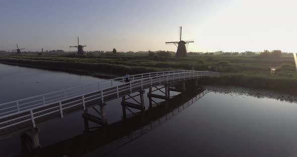 A drone shot panning right, around a girl walking and turning around on a bridge, looking at Dutch W