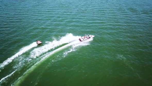 Drone shot of a boat pulling a tube with two people on it. The boat is going fast and almost causes